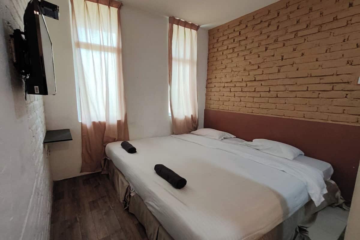 A room with two beds, a brick wall, and a mounted TV.