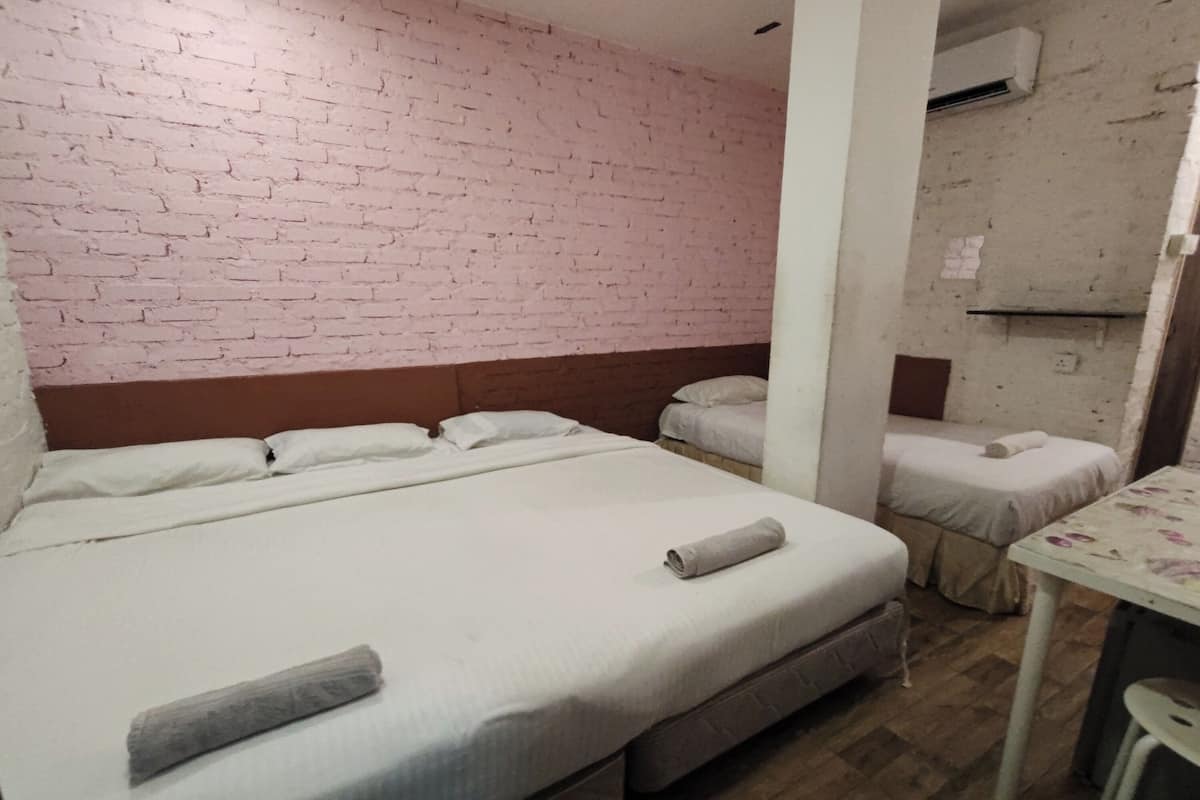 A hotel room with a brick wall, a large bed with a wooden headboard, two smaller beds, a table, and an air conditioning unit.