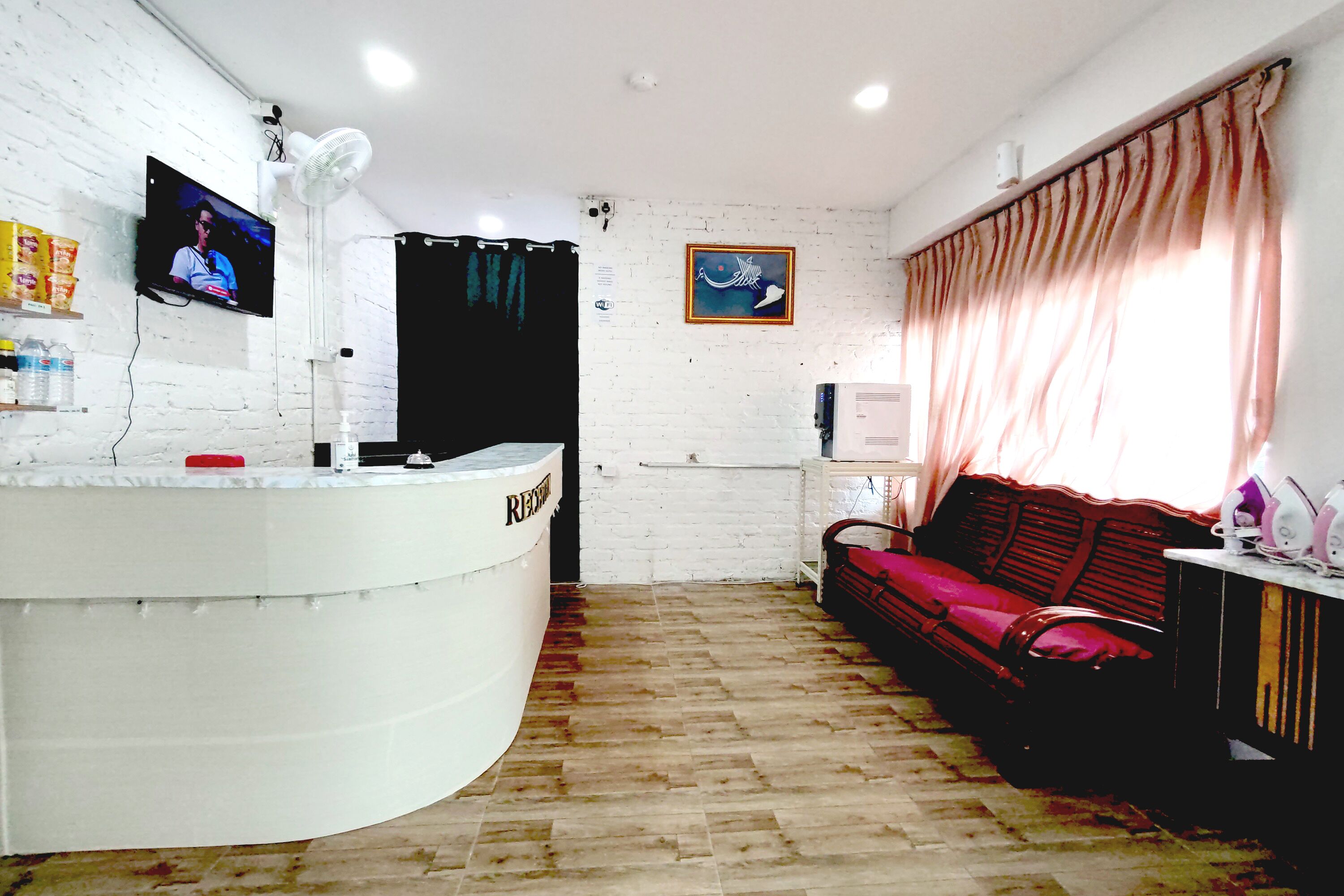 A reception area with a white reception desk, a television mounted on the wall, a red sofa, and a window with curtains.