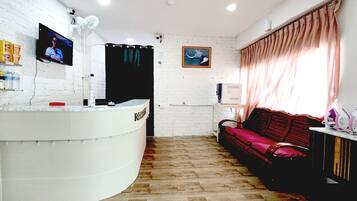 A reception area with a white reception desk, a television mounted on the wall, a red sofa, and a window with curtains.