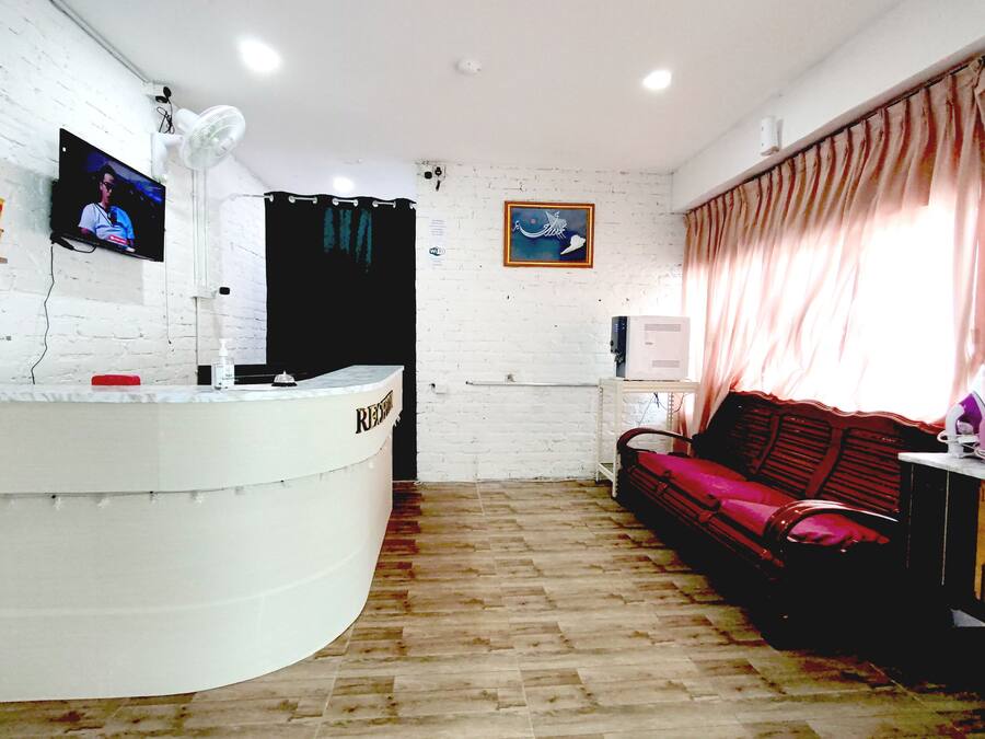 A reception area with a white reception desk, a television mounted on the wall, a red sofa, and a window with curtains.
