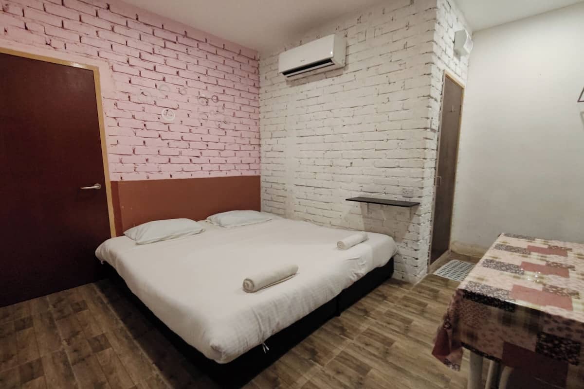A room with a bed, a table, an air conditioning unit, and a brick-patterned wall.