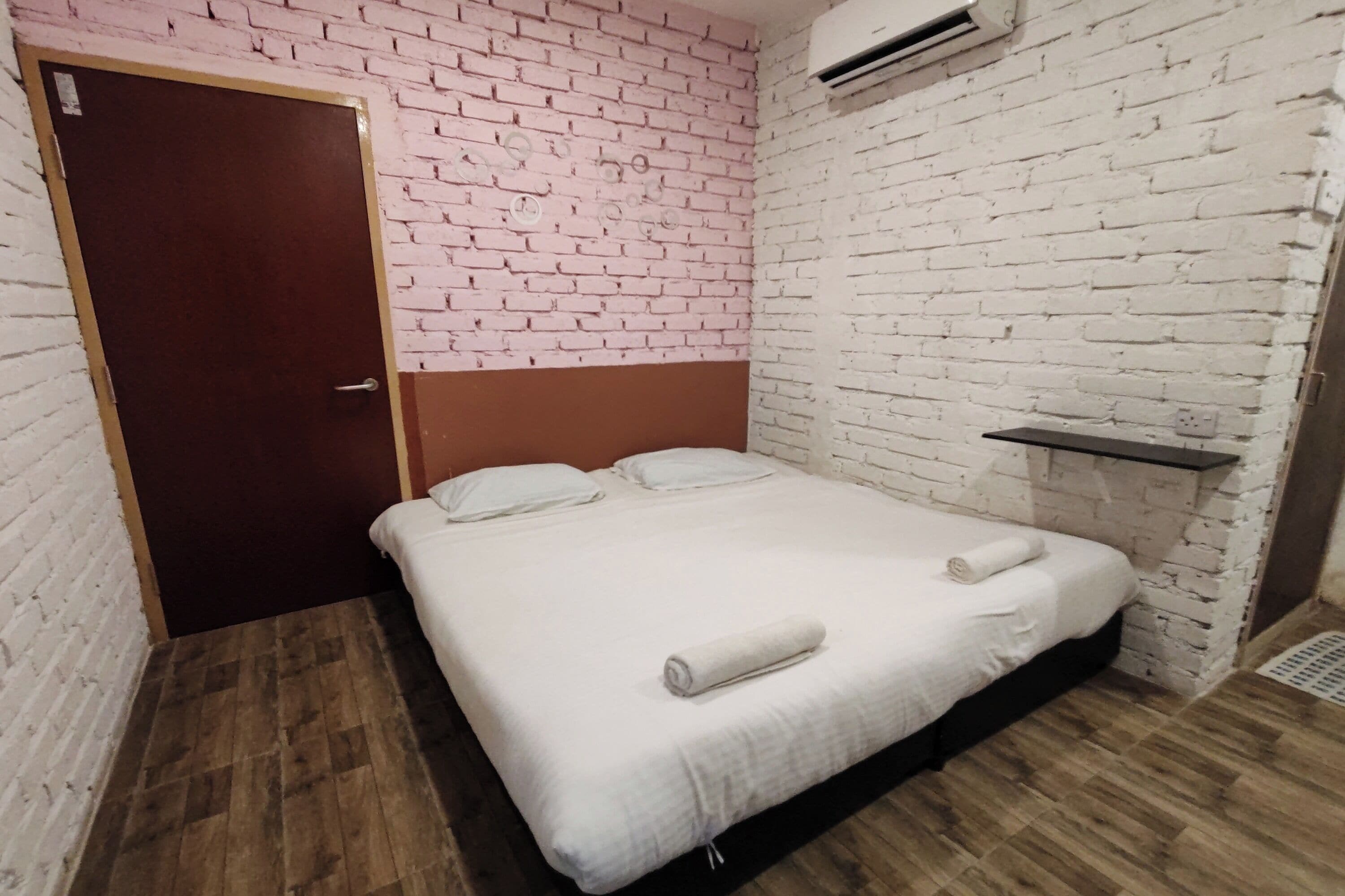 A room with a bed, a wooden floor, a brick wall, and a door.