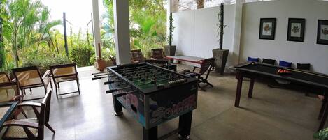 A room with a foosball table, a pool table, and several chairs.