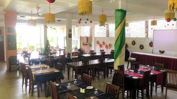 Uma sala de jantar com várias mesas preparadas para hóspedes, apresentando diferentes opções de assento e um ambiente festivo com decorações penduradas.