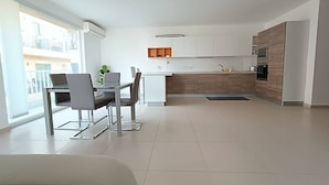 A modern kitchen with white cabinets, a wooden countertop, and a built-in oven. There is a dining area with a table and chairs, and a large window providing natural light. - This apartment is a 2 bedroom(s), 2 bathrooms, located in Il-Mellieħa, null. (Il-Mellieħa)