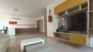 A modern living room with a flat-screen TV, a guitar, and a minimalist design. - This apartment is a 2 bedroom(s), 2 bathrooms, located in Il-Mellieħa, null. (Il-Mellieħa)