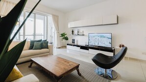 A modern living room with a sofa, coffee table, and a black chair. There is a TV on a stand and a plant on the windowsill. - Escape to your dream coastal retreat in Mellieħa — a spacious, modern haven just steps from golden beaches. Relax, unwind, and soak up the island sunshine. (Il-Mellieħa)