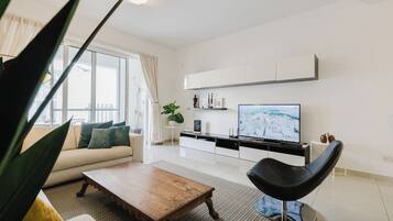 A modern living room with a sofa, coffee table, and a black chair. There is a TV on a stand and a plant on the windowsill.
