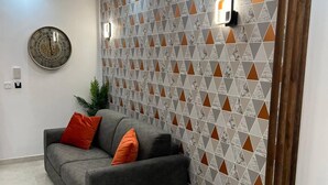 Una sala moderna con un sofá gris, cojines naranjas, una mesa de centro redonda y una pared con diseño.