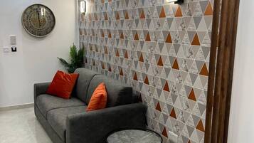 Ein modernes Wohnzimmer mit einem grauen Sofa, orangefarbenen Kissen, einem runden Couchtisch und einer Wand mit Muster.