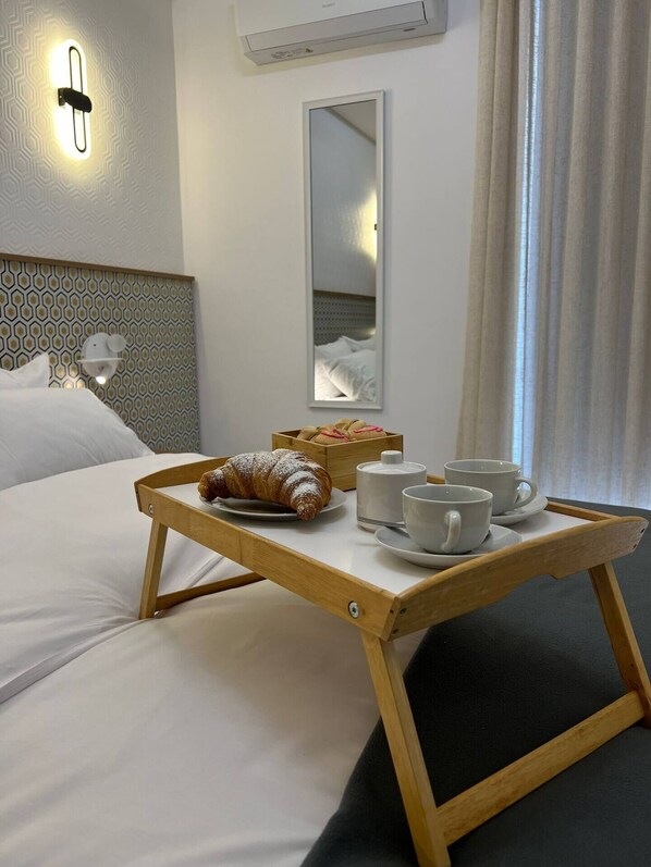 A hotel room with a bed, a tray with croissants, cups, and a box of cookies.