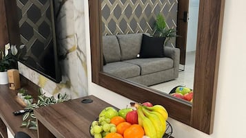 Uma sala de estar moderna com uma escrivaninha de madeira, uma tigela de frutas, uma televisão e um sofá.