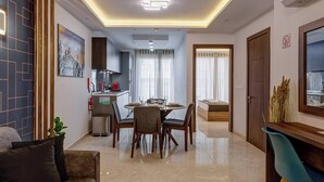 A modern living room with a sofa, a dining area with a table and chairs, a kitchen in the background, and a hallway leading to a bedroom. - A modern apartment block in the heart of Bugibba. All one-bedroom flats, stylishly finished and fully equipped with comfort, ideally located close to shops, services, and all amenities. (San Pawl il-Baħar)