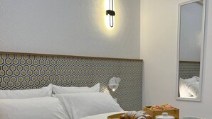A neatly made bed with white linens, a bedside table with a tray of croissants, cups, and a small container, and a wall-mounted light fixture. - A modern apartment block in the heart of Bugibba. All one-bedroom flats, stylishly finished and fully equipped with comfort, ideally located close to shops, services, and all amenities. (San Pawl il-Baħar)
