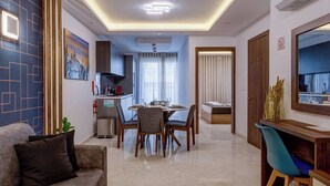 Una sala de estar moderna con sofá, mesa de comedor y sillas, una zona de cocina y un dormitorio con cama y cortinas.