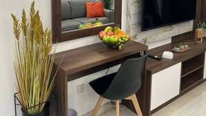 A modern living room with a flat-screen TV, a wooden desk, a comfortable sofa, and a decorative mirror.
