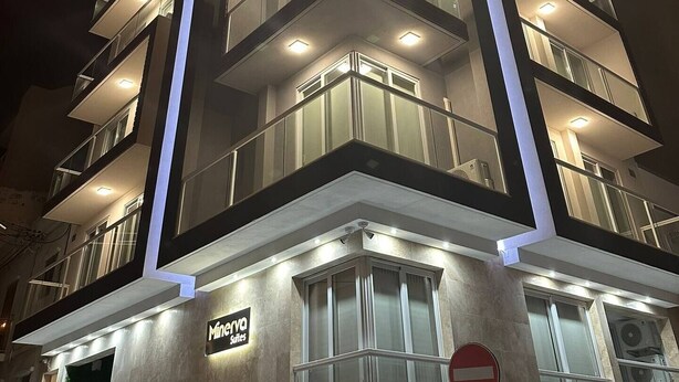 A multi-story hotel with a modern design, featuring balconies on each floor, a sign indicating 'Minerva Suites', and a no-entry traffic sign.