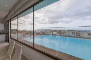 Un interior moderno con un amplio ventanal que ofrece vistas a una piscina en la azotea y al paisaje urbano.