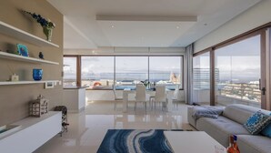 A modern living room with a large window, a dining area, and a sofa with a view of the city.