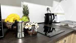 Una encimera de cocina con una cafetera, un tarro de crema de chocolate, una cesta de frutas y un hervidor.