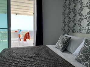 Un dormitorio con una cama grande, un cabecero estampado y vistas a un balcón con mobiliario exterior.
