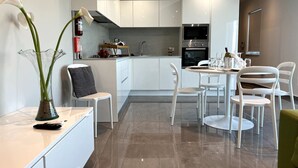 A modern kitchen with white cabinets, a dining area with white chairs, and a vase with flowers on the counter. - Take it easy and soak up the good life at this unique luxury penthouse, where sweeping sea views and your own rooftop pool make every moment feel unforgettable. (Il-Mellieħa)
