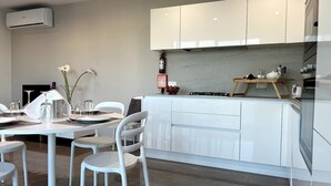 A modern kitchen with white cabinetry, a built-in stove, and a dining area with white chairs and a table set for two. - Take it easy and soak up the good life at this unique luxury penthouse, where sweeping sea views and your own rooftop pool make every moment feel unforgettable. (Il-Mellieħa)