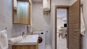 A modern bathroom with a sink, mirror, towel rack, and a washing machine.