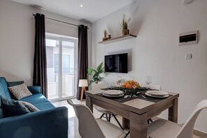 Un salon moderne avec un canapé bleu, une table à manger dressée pour quatre personnes et un téléviseur fixé au mur.