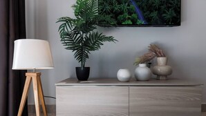 A modern living room with a light wood cabinet, a potted plant, a floor lamp, and decorative vases. - This apartment is a 2 bedroom(s), 1 bathrooms, located in Il-Mellieħa, null. (Il-Mellieħa)