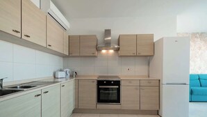 Eine moderne Küche mit hellen Holzschränken, einem eingebauten Ofen, einer Spülmaschine und einem weißen Kühlschrank.