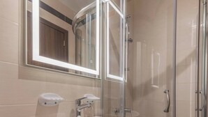 Ein modernes Badezimmer mit einem weißen Waschbecken, einer Glasdusche und einem großen Spiegel mit LED-Beleuchtung.