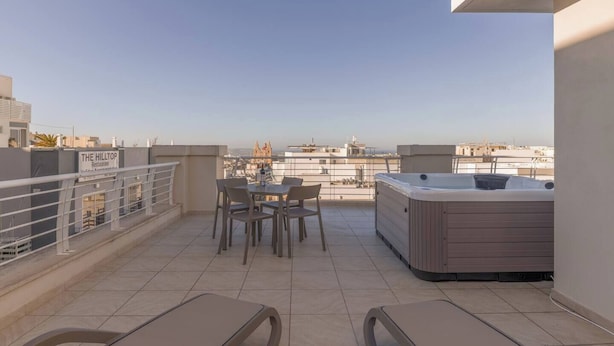 Eine Dachterrasse mit Tisch und Stühlen, einem Whirlpool und Blick auf die Stadtlandschaft.