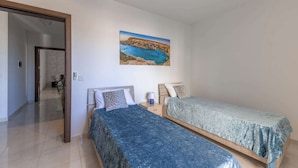 Ein Schlafzimmer mit zwei Betten, einem Gemälde einer Küstenlandschaft und einer Tür zu einem anderen Raum.