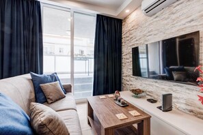 Una sala de estar moderna con un sofá, una mesa de centro de madera y un televisor grande sobre una pared con textura.