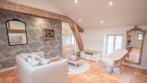 A spacious living room with a white sofa, a coffee table, and a chair. The room features exposed wooden beams, a patterned wallpaper, and a large mirror. - Le Cadran Solaire, Gîte Intimiste Haut de Gamme Avec Piscine et Sauna, à Pézenas (Pézenas)