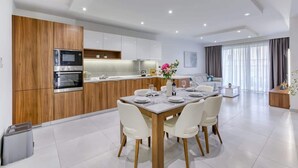 A modern kitchen with wooden cabinets, stainless steel appliances, and a dining area with a marble table and white chairs.
