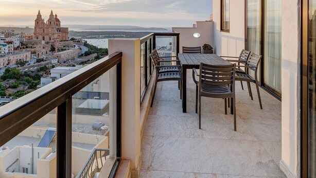Un balcon avec une table et des chaises, donnant sur un bâtiment historique et sur une étendue d’eau.