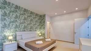 Une chambre moderne avec un grand lit, deux tables de chevet blanches, une lampe de chevet et une armoire.
