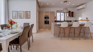 Une cuisine moderne dotée d’un îlot central, de tabourets de bar blancs et d’un coin repas avec une table dressée pour quatre personnes.
