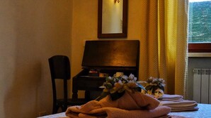 Une chambre d’hôtel avec un lit, une chaise, un bureau avec une lampe, un miroir et une fenêtre avec des rideaux.