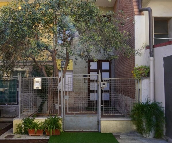 A fenced courtyard with a tree, a gate, and potted plants. - B&B Myosotis (Pisa)