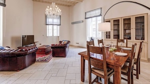 A spacious living room with a leather sofa, a wooden dining table set for four, and a chandelier.