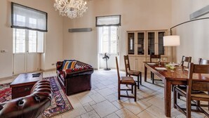 A spacious living room with a leather sofa, a dining table set for four, and a chandelier.