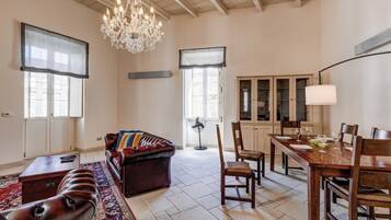 Uma sala de estar espaçosa com um sofá de couro, uma mesa de jantar posta para quatro pessoas e um lustre.