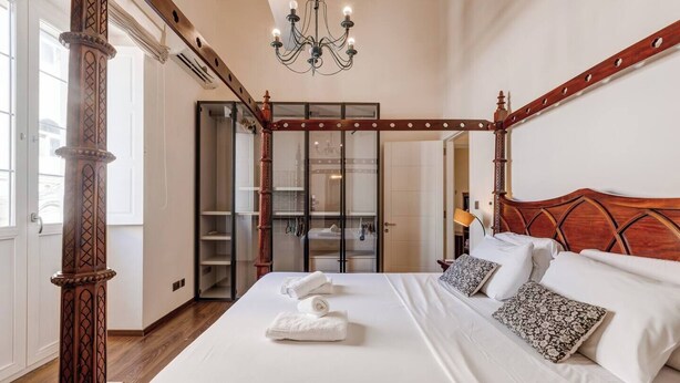 A four-poster bed with white linens, a chandelier, and a wooden headboard.