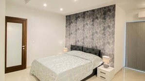 A modern bedroom with a large bed, a dark headboard, and a textured wall behind it. - This apartment is a 2 bedroom(s), 2 bathrooms, located in Il-Mellieħa, null. (Il-Mellieħa)