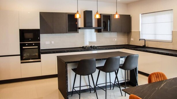 A modern kitchen with a central island, black bar stools, and pendant lighting. - This apartment is a 2 bedroom(s), 2 bathrooms, located in Il-Mellieħa, null. (Il-Mellieħa)