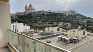 A rooftop terrace with large water tanks, a glass balustrade, and a view of a historic building on a hill. - This apartment is a 2 bedroom(s), 2 bathrooms, located in Il-Mellieħa, null. (Il-Mellieħa)